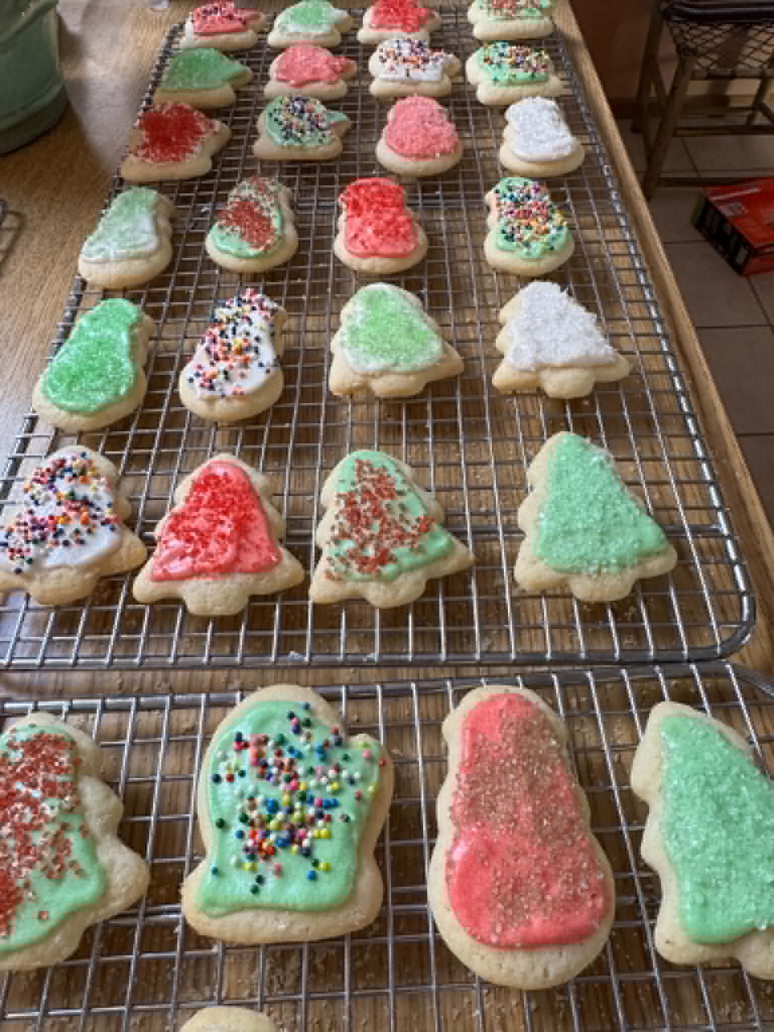 Frosted red and green Christmas cutout cookies with sprinkles cooling on wire racks