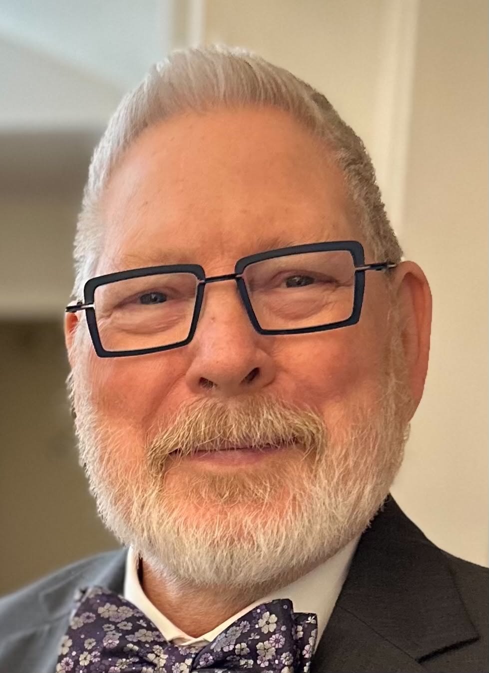Portrait of Dale Rice — silver beard, dark rectangular glasses, and a floral bow tie