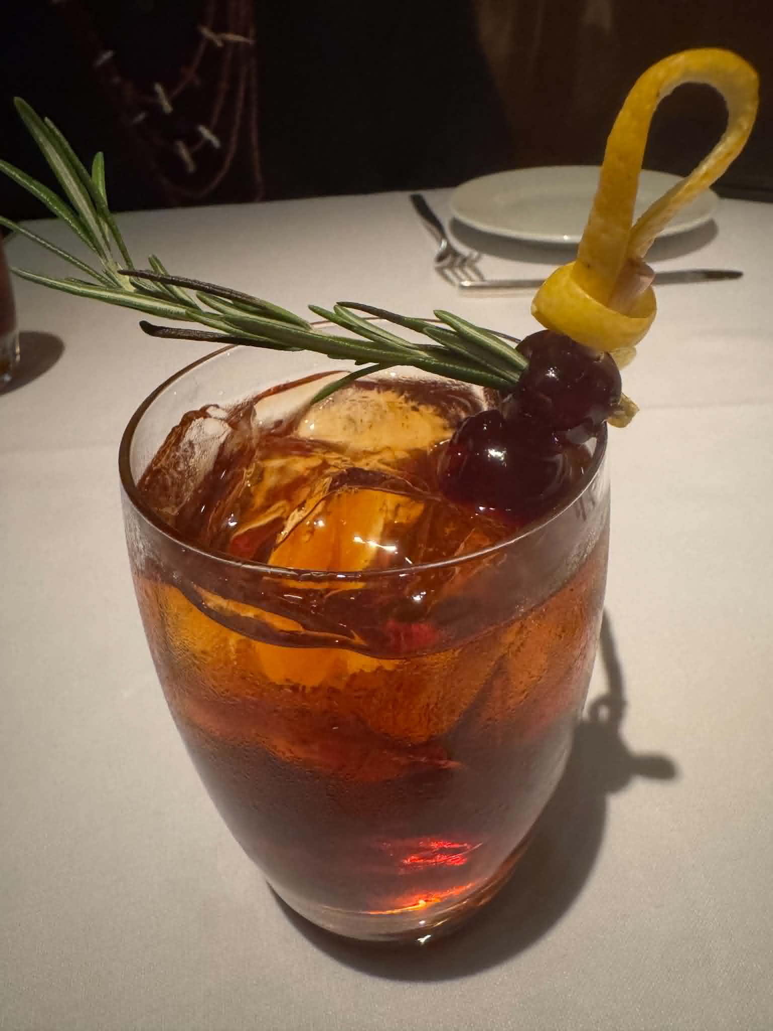 A cocktail garnished with a rosemary sprig, skewered cherries, and a citrus twist at Geronimo