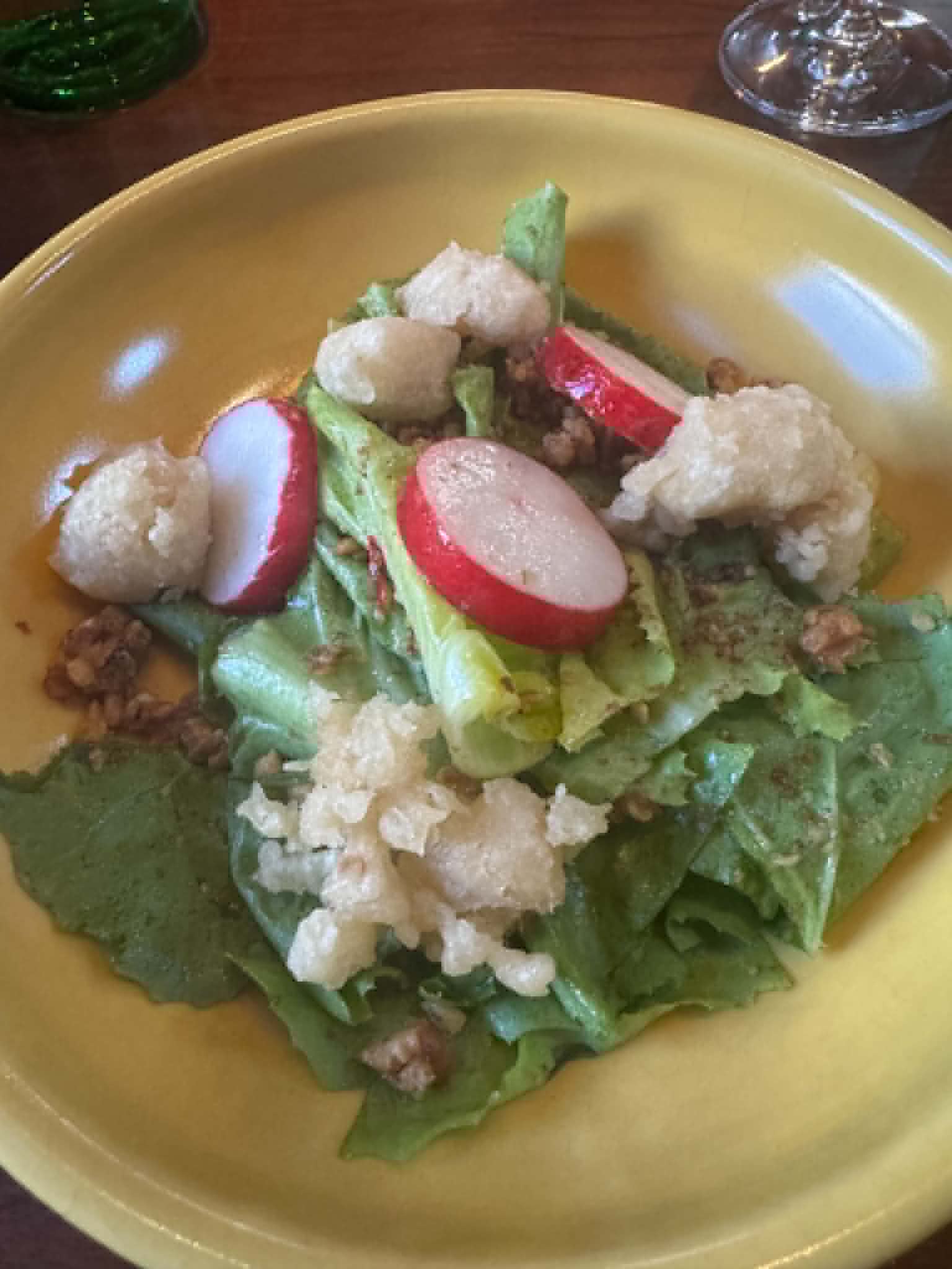 Butter lettuce salad with sliced radishes, crispy fried bits, and toasted walnuts on a yellow plate